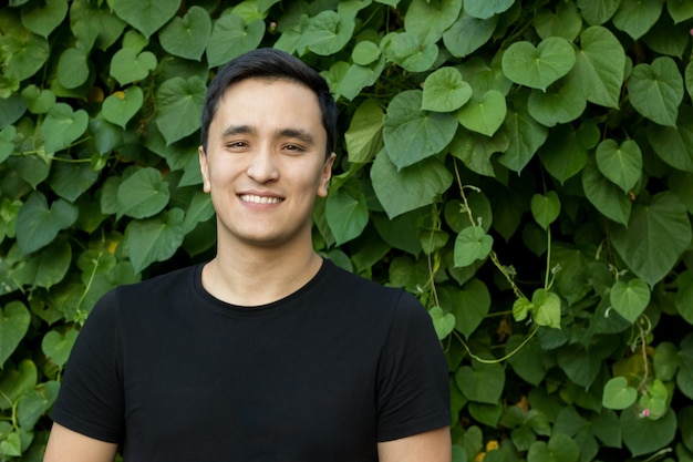 Jeune homme asiatique en t-shirt noir sur fond de belle plante verte, mode de vie sain.