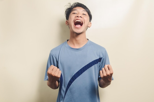 Jeune homme asiatique en t-shirt de sport avec une expression triomphante isolée sur fond