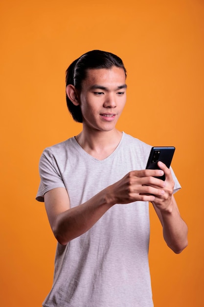 Jeune homme asiatique tapant un message sur smartphone, concept de communication en ligne. Adolescent gai debout, naviguant sur Internet sur un téléphone portable, personne séduisante utilisant les médias sociaux