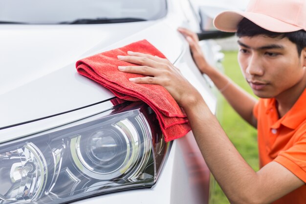 Jeune homme asiatique en utilisant un chiffon microfibre rouge nettoyage corps de la nouvelle voiture argentée