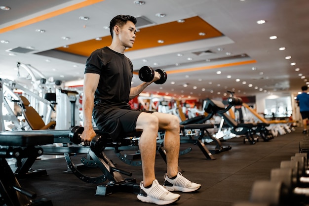 Jeune homme asiatique utilisant des exercices d'haltères au gymnase pour une bonne santé dans la forme physique Concept d'exercice de style de vie et de sport