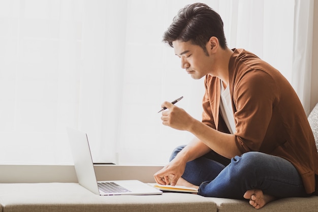 Jeune homme asiatique utilisant un ordinateur portable et écrivant dans un ordinateur portable.