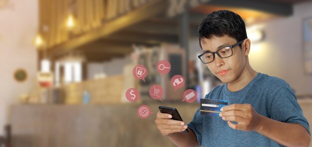 Jeune homme asiatique utilisant un smartphone avec une carte de crédit avec l'icône de la boutique en ligne. Concept d'achat en ligne.