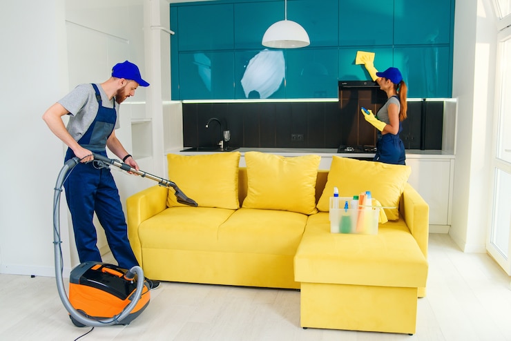 Photo jeune homme avec aspirateur laver avec canapé jaune vapeur et belle femme essuie les meubles de cuisine.