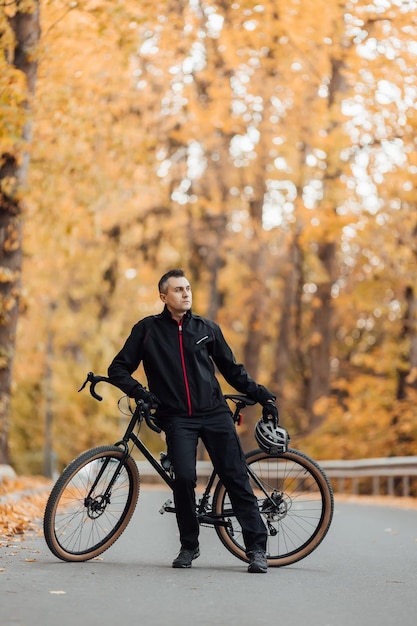 Jeune homme assez athlétique debout avec vélo dans le parc d'automne