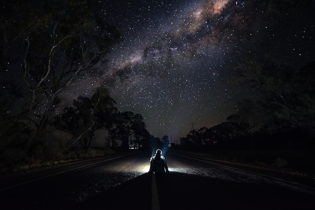 Jeune homme assis sur l'autoroute la nuit en regardant la voie lactée. Concept de photographie de voyageur et d'astro