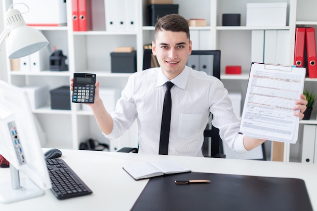 Un jeune homme assis à un bureau d'ordinateur dans le bureau et tenant une tablette et une calculatrice.