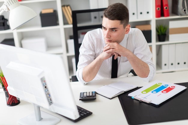 Un jeune homme assis à un bureau d'ordinateur dans le bureau et travaillant avec des documents.