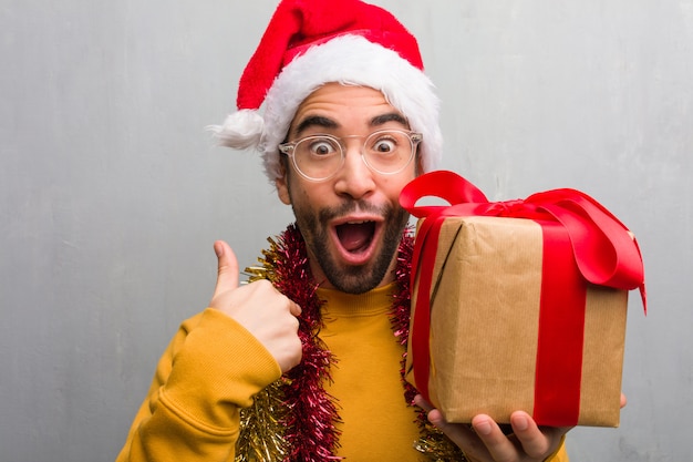 Jeune homme assis avec des cadeaux célébrant Noël surpris, sent réussi et prospère