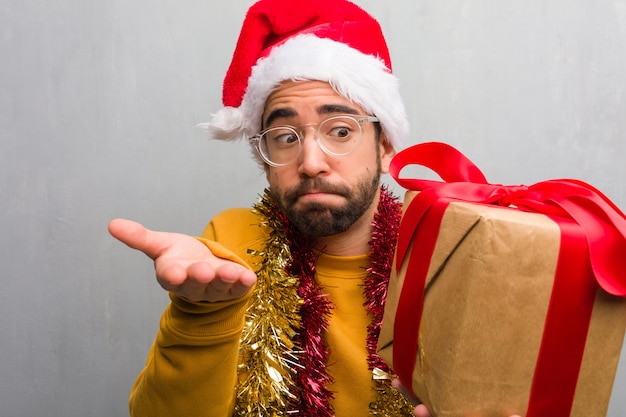 Jeune homme assis avec des cadeaux pour célébrer Noël confus et douteux