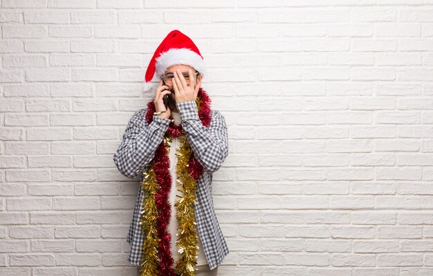 Jeune homme assis avec des cadeaux pour célébrer Noël embarrassé et rire en même temps