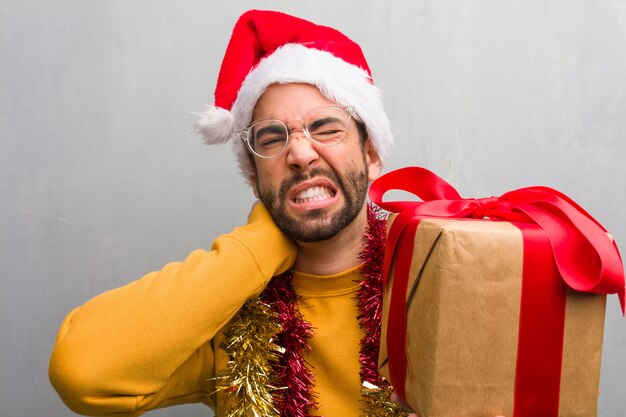 Jeune homme assis avec des cadeaux pour célébrer Noël souffrant de douleurs au cou