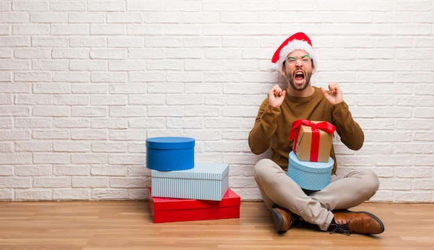 Jeune homme assis avec des cadeaux pour fêter Noël en criant très en colère et agressif