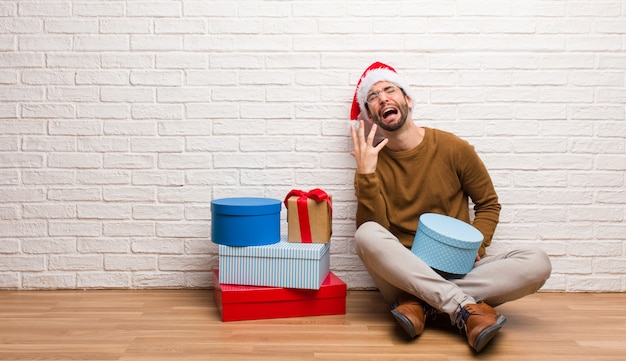 Jeune homme assis avec des cadeaux pour fêter Noël très effrayé et effrayé