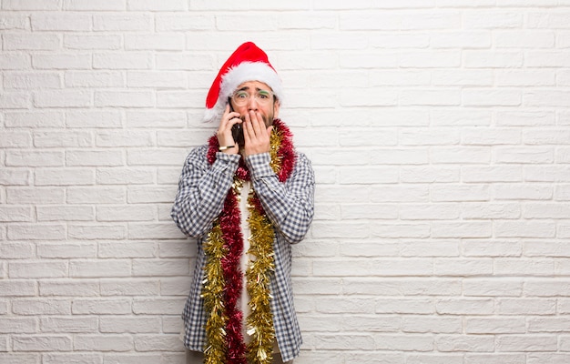 Jeune homme assis avec des cadeaux pour fêter Noël très effrayé et peur caché