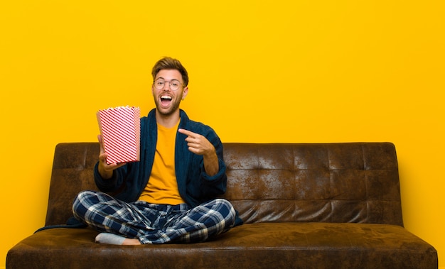 Jeune homme assis sur un canapé avec des popcorns. cinéma