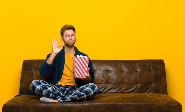 Jeune homme assis sur un canapé avec des popcorns.