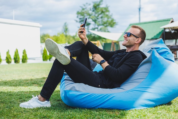 Photo jeune homme assis sur une chaise à l'extérieur et parler au téléphone indépendant masculin de travail à distance