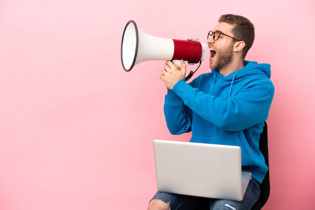 Jeune homme assis sur une chaise avec un ordinateur portable criant à travers un mégaphone