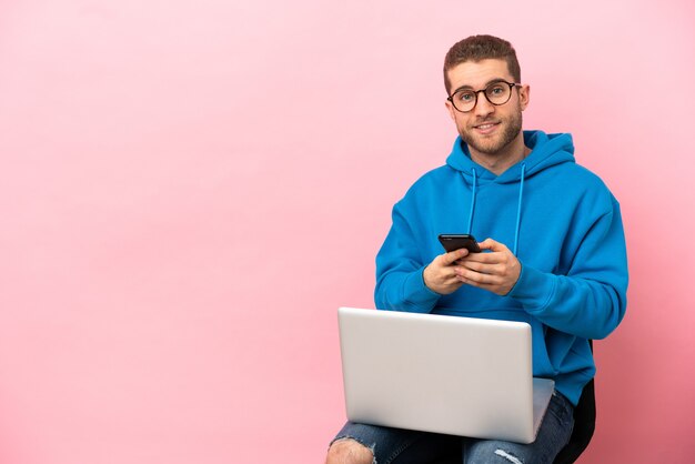 Jeune homme assis sur une chaise avec ordinateur portable l'envoi d'un message avec le mobile