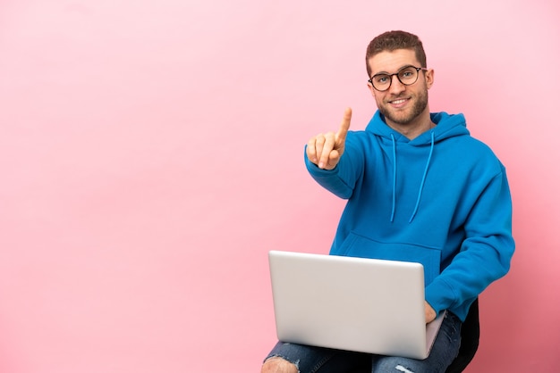 Jeune homme assis sur une chaise avec ordinateur portable montrant et levant un doigt