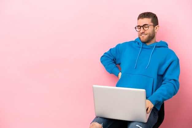 Jeune homme assis sur une chaise avec ordinateur portable souffrant de maux de dos pour avoir fait un effort