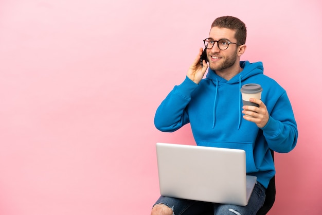 Jeune homme assis sur une chaise avec un ordinateur portable tenant du café à emporter et un mobile