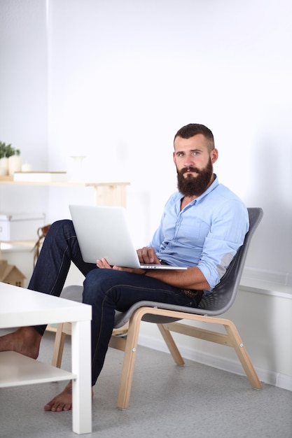 Jeune homme assis sur une chaise et travaillant sur un ordinateur portable isolé sur fond blanc