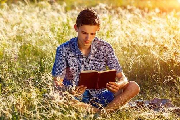 Jeune homme assis dans la nature en lisant un livre