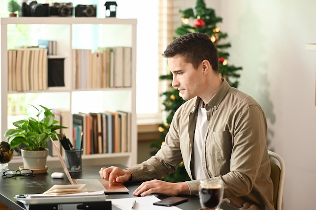 Jeune homme assis dans le salon et travaillant avec un ordinateur portable