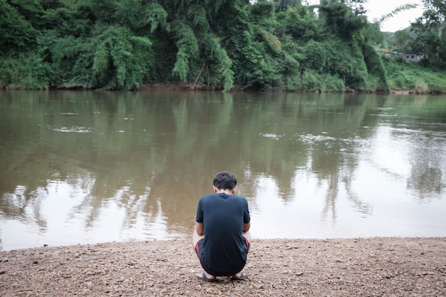 Photo jeune homme assis devant le lac