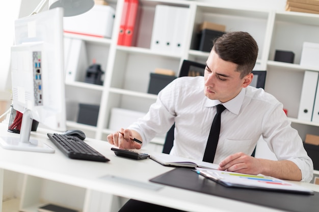 Un jeune homme assis devant un ordinateur Bureau dans le bureau et travaillant avec des documents.