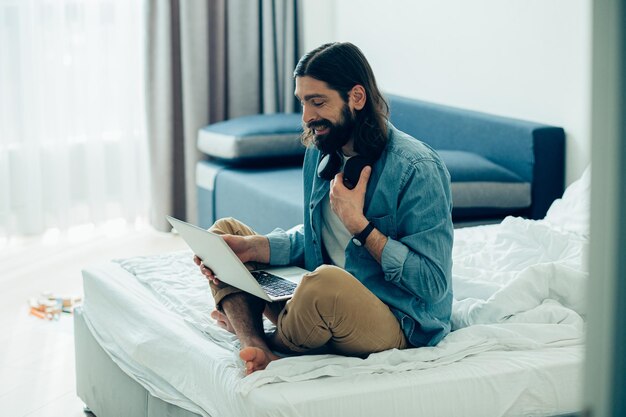 Jeune homme assis sur le lit avec un ordinateur portable et parlant à des proches en ligne pendant la quarantaine