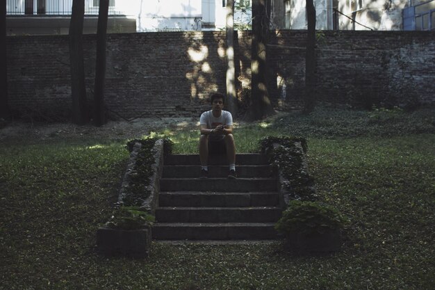 Photo jeune homme assis sur les marches du parc