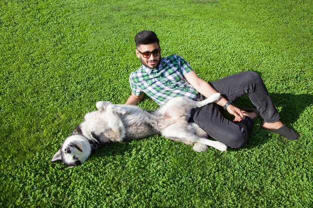Jeune homme assis sur une pelouse verte et s'amusant avec son chien
