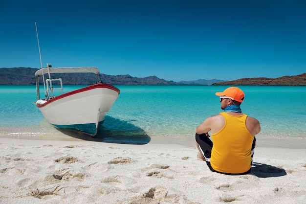 Jeune homme assis sur la plage paradisiaque de sable blanc mer turquoise et ciel bleu Playa Isla Coronado Mexique