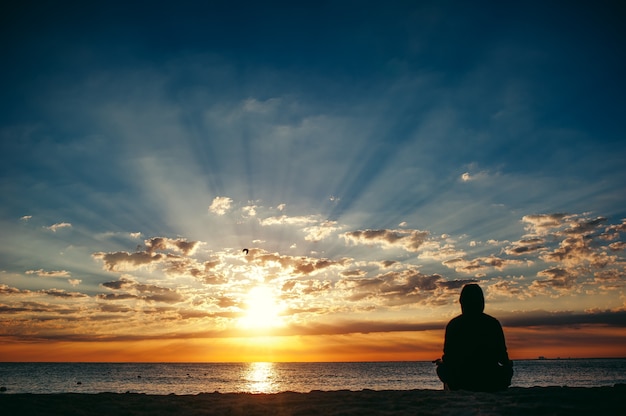 Jeune homme assis sur la plage et pratiquant la sérénité et le yoga au lever du soleil