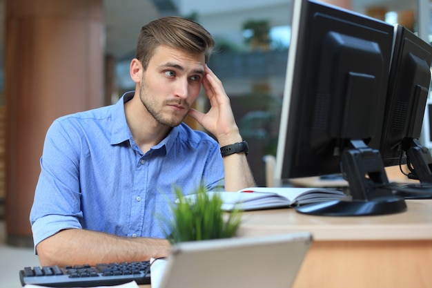 Jeune homme assis et regardant un écran d'ordinateur tout en travaillant au bureau.