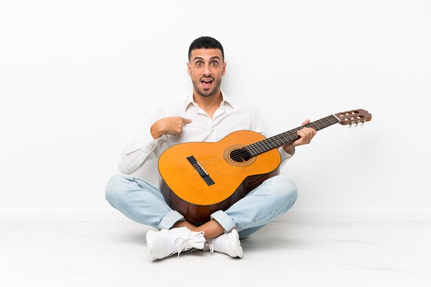 Jeune homme assis sur le sol avec une guitare avec une expression faciale surprise