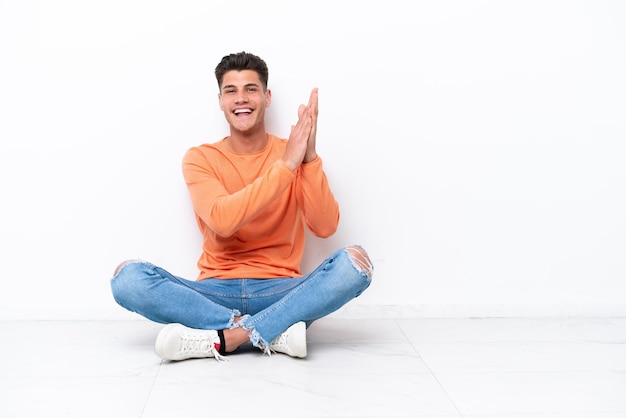 Jeune homme assis sur le sol isolé sur fond blanc applaudissant après présentation lors d'une conférence