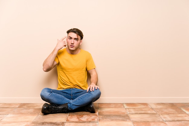 Jeune homme assis sur le sol montrant un geste de déception avec l'index