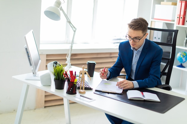 Un Jeune Homme Assis à Une Table Dans Le Bureau Tient Un Stylo Rouge à La Main Et Travaille Avec Des Documents.