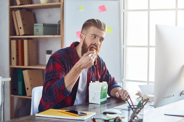 Jeune homme assis à la table du bureau et prenant la pause déjeuner