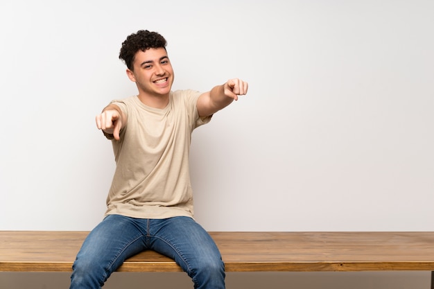 Jeune homme assis sur une table montre du doigt en souriant