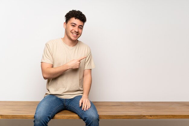 Jeune homme assis sur une table pointant sur le côté pour présenter un produit