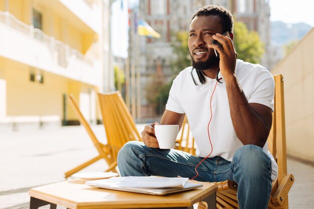 Jeune homme assis sur une terrasse et prendre un café