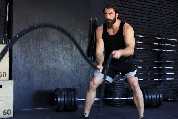 Jeune homme athlétique avec corde de combat faisant de l'exercice dans une salle de fitness d'entraînement fonctionnel.