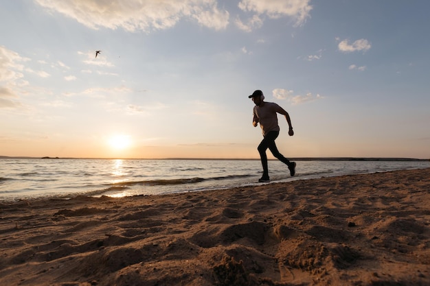 Jeune homme athlétique courant le long d'une plage de sable