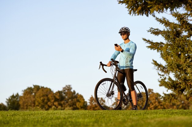 Jeune homme athlétique cycliste professionnel en vêtements de sport et casque de protection debout avec son vélo