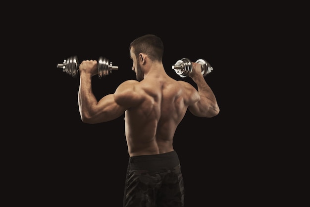 Photo jeune homme athlétique avec haltère sur fond noir, faisant des exercices de force biceps. torse nu, corps musclé, concept de musculation, espace de copie